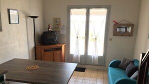 Un espacio habitable compacto con una mesa de comedor, un sofá, un televisor sobre un soporte de madera y una pequeña cocina.