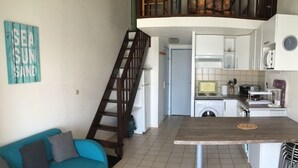 Un espacio habitable compacto con kitchenette, un sofá y una escalera que conduce a un nivel superior.