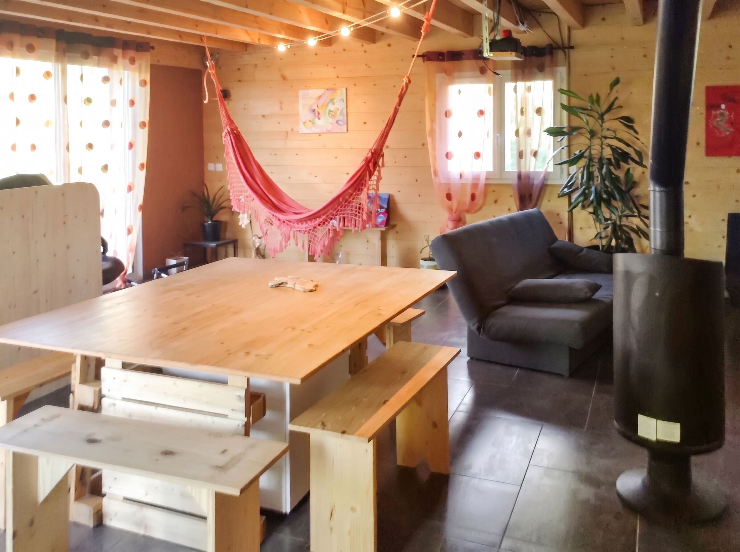 Un intérieur en bois avec une grande table, des bancs, un canapé, un hamac et une cheminée.