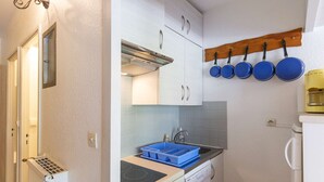A compact kitchen with white cabinets, a built-in oven, a dishwasher, and a blue dish rack. - Lovely studio for 6 people at the foot of the slopes (Gourette)