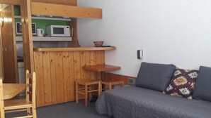 Een compacte kamer met een kitchenette, een bank, een stoel en een klein tafeltje.
