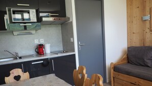 A compact kitchen with a microwave, coffee maker, and a sink. There is a wooden table with chairs and a grey sofa. - Renovated studio near slopes with balcony (Les Menuires)