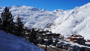 A snow-covered mountain with a clear blue sky. There are buildings and parked cars in the foreground. - Renovated studio near slopes with balcony (Les Menuires)