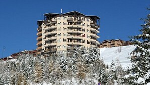 A multi-story hotel with balconies, surrounded by snow-covered trees and a clear blue sky. - Renovated studio near slopes with balcony (Les Menuires)