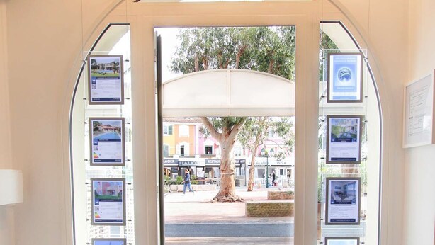 An entrance with a blue mat, framed pictures on the walls, and a view of the street outside.