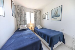 Una habitación con dos camas individuales, una ventana con cortinas, un cuadro colgado en la pared y una mesita de noche con lámpara.