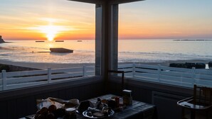 A room with a view of the ocean at sunset, a dining table with various items, and a white railing. - Homerez - House in Arromanches-les-Bains (Arromanches-les-Bains)
