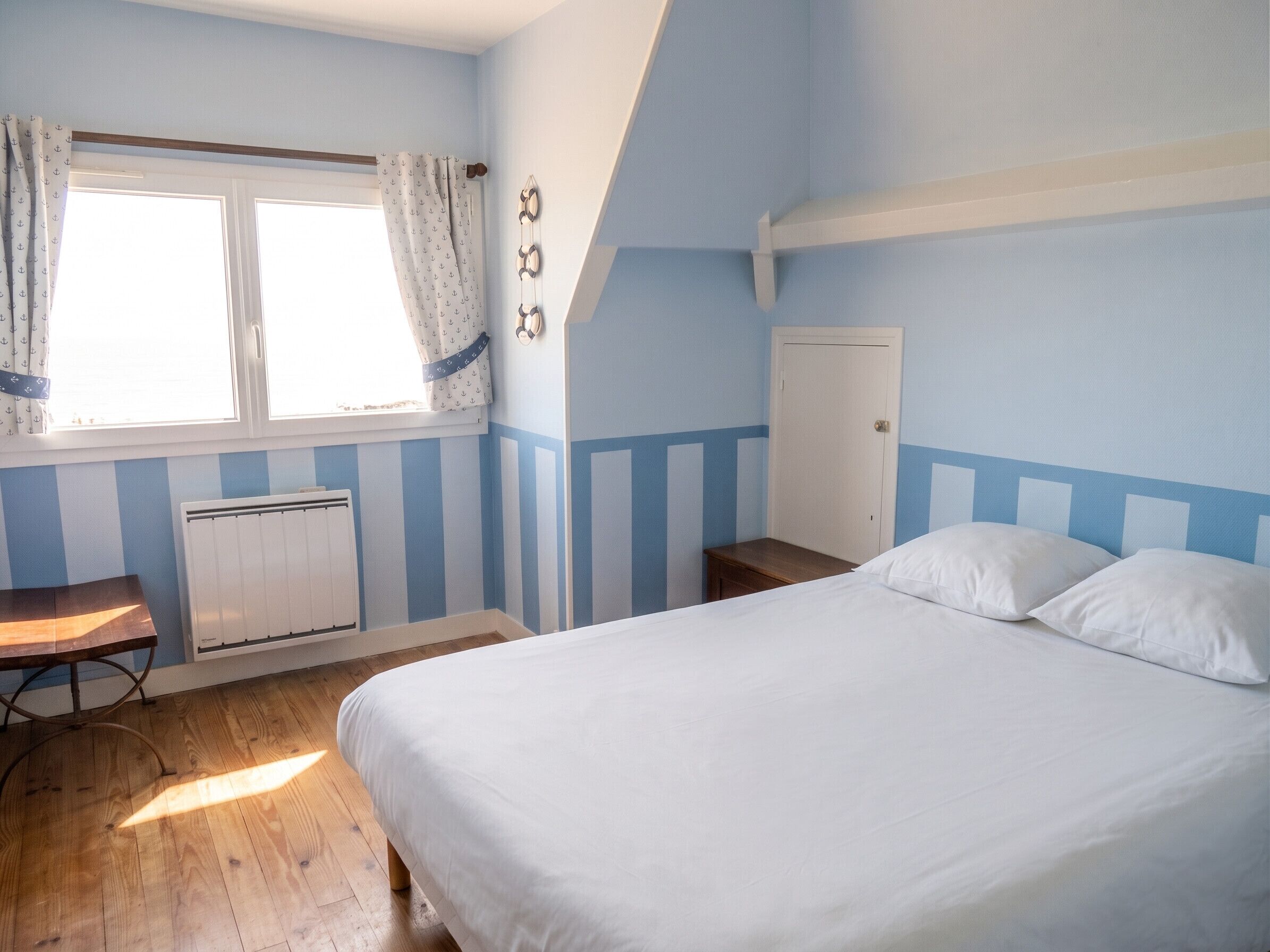Une chambre à coucher avec un lit, une fenêtre avec des rideaux, un radiateur et un plancher en bois.