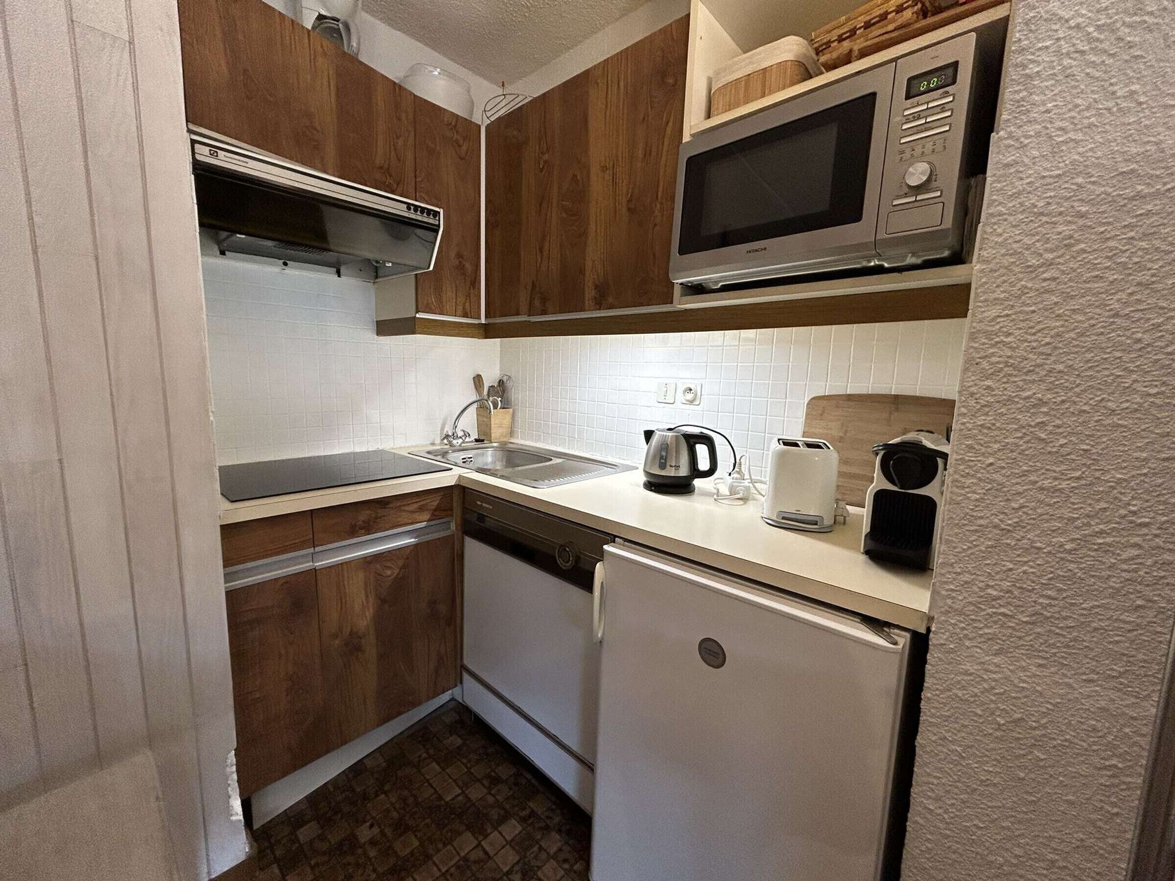 A compact kitchen with wooden cabinets, a microwave, a kettle, and a toaster.