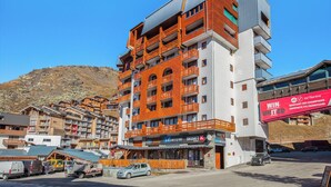 Un hotel de varios pisos con balcones, tiendas de esquí y un telesilla al fondo.