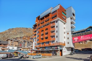 Un hôtel à plusieurs étages doté de balcons, de boutiques de ski et, au loin, d’un télésiège.