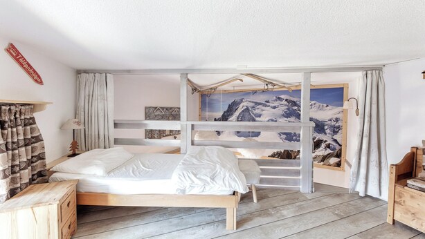 Un dormitorio con una cama de madera, una mesita de noche, una lámpara y vistas a montañas a través de una ventana.