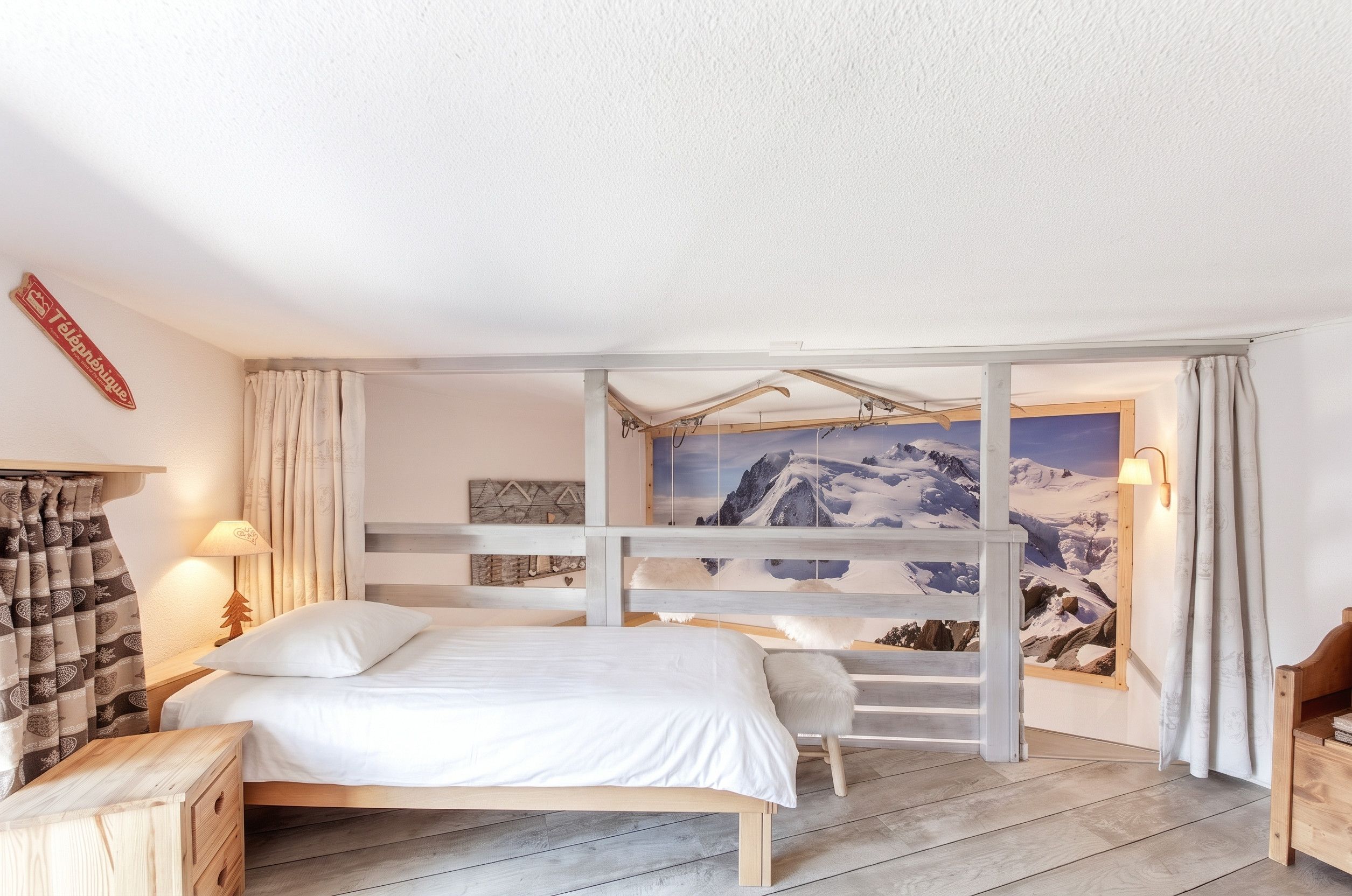 A bedroom with a bed, a wooden headboard, a mountain view painting, and a wooden dresser.