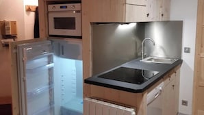 Una cocina compacta con armarios de madera, horno empotrado, pileta de acero inoxidable y refrigerador.