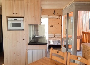 Une petite cabane en bois comprenant un coin cuisine, un lit et un espace repas.
