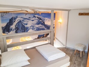 Une pièce comprenant un lit, un tableau représentant un paysage de montagne, un petit tabouret et un luminaire fixé au mur.