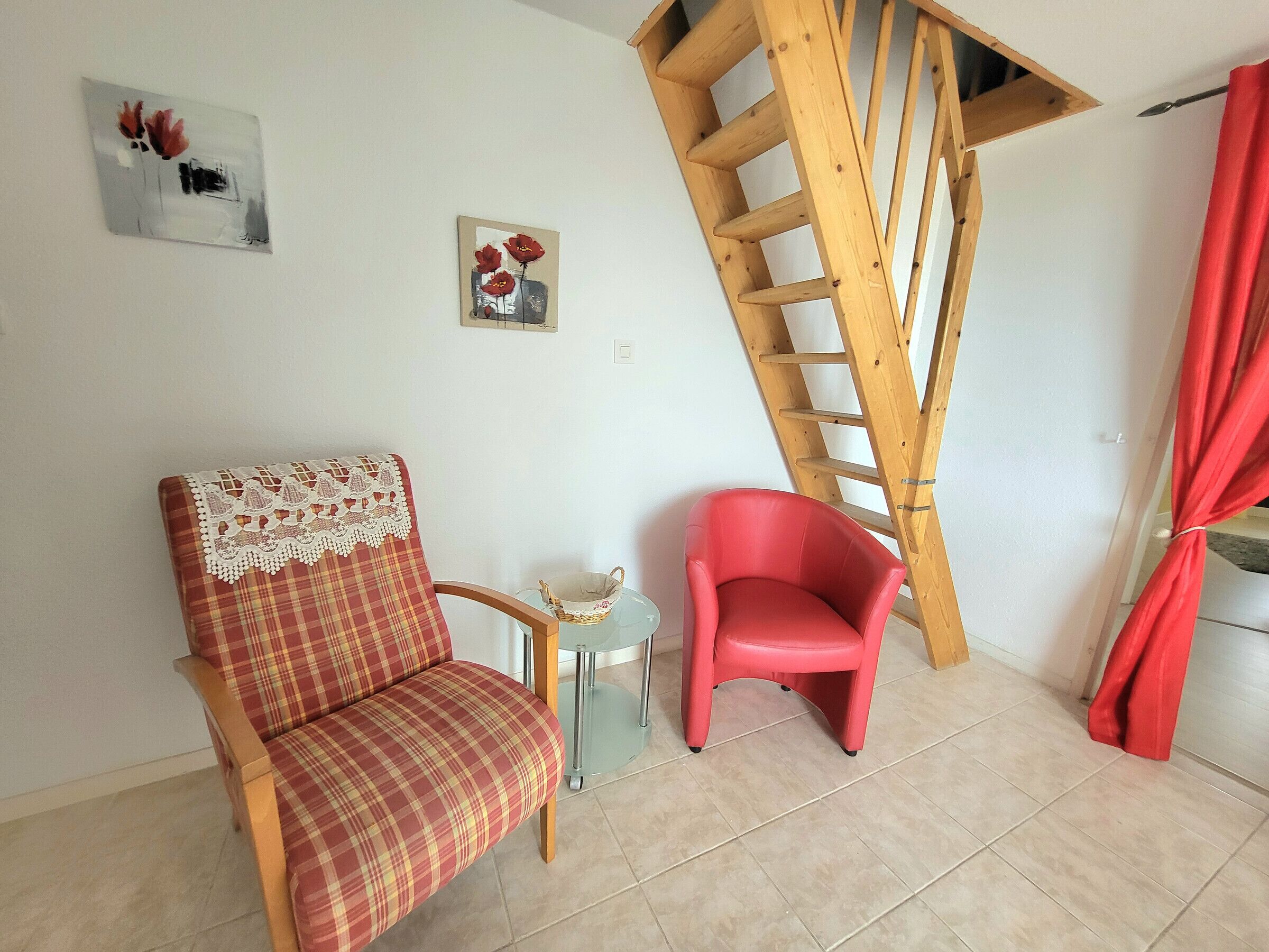 A room with a plaid chair, a red chair, a small table with a basket, and a wooden ladder against the wall.