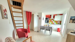 A compact living space with a dining area, kitchenette, and a loft bedroom with a wooden ladder.