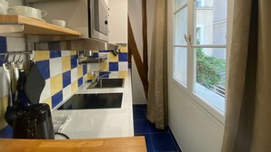 Une cuisine compacte équipée d’un four à micro-ondes, d’un évier et d’ustensiles de cuisine. Une fenêtre avec des rideaux offre une vue sur la verdure environnante.