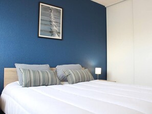 A hotel room with a bed, two striped pillows, a nightstand with a lamp, and a framed picture on the wall.