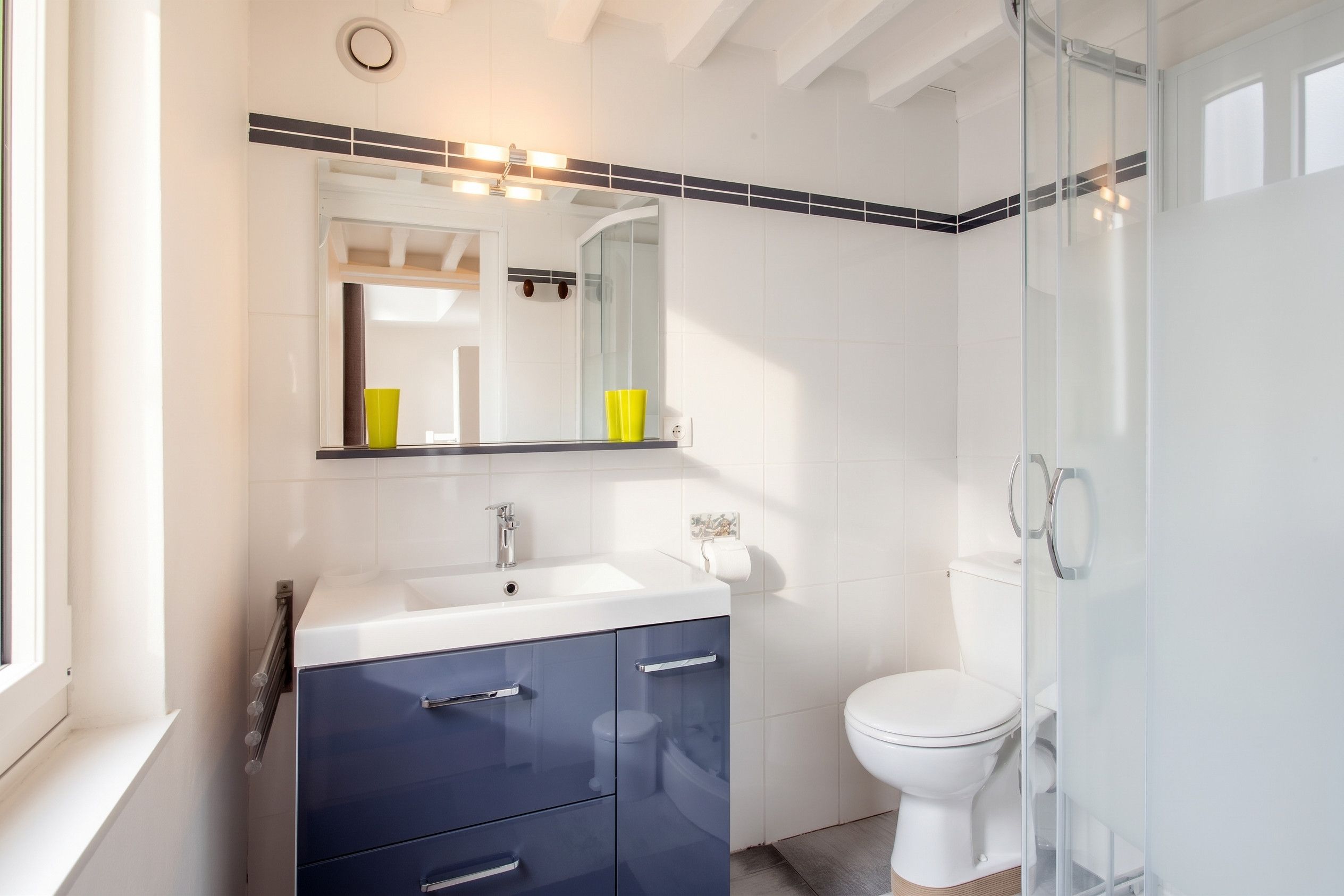 A modern bathroom with a white sink, dark blue cabinets, a glass shower enclosure, and a white toilet.