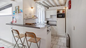 A compact kitchen with a bar area, white cabinetry, a microwave, and a radiator. - Homerez - Charming House near Sainte Catherine (Honfleur)
