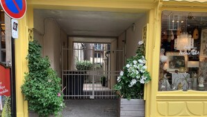 A storefront with a yellow facade, a metal gate, and potted plants. - Homerez - Charming House near Sainte Catherine (Honfleur)