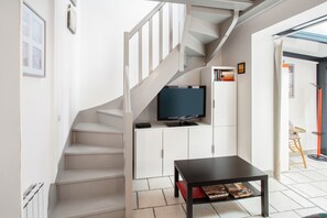 A modern interior with a staircase, a flat-screen TV, a small table, and a bookshelf.