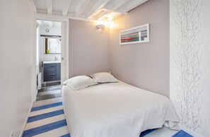 A bedroom with a bed, a bedside table, a wall-mounted light, and a door leading to a bathroom.