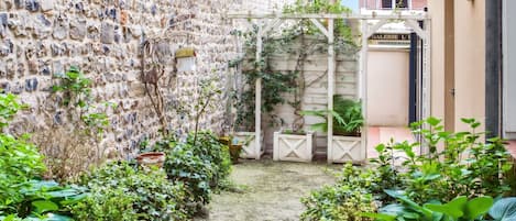 Une cour intérieure avec un mur en pierre, des plantes en pot et une pergola en bois.