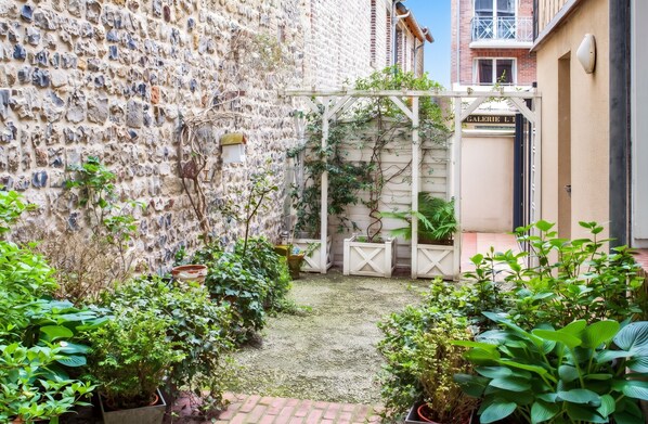A courtyard with a stone wall, potted plants, and a wooden pergola.