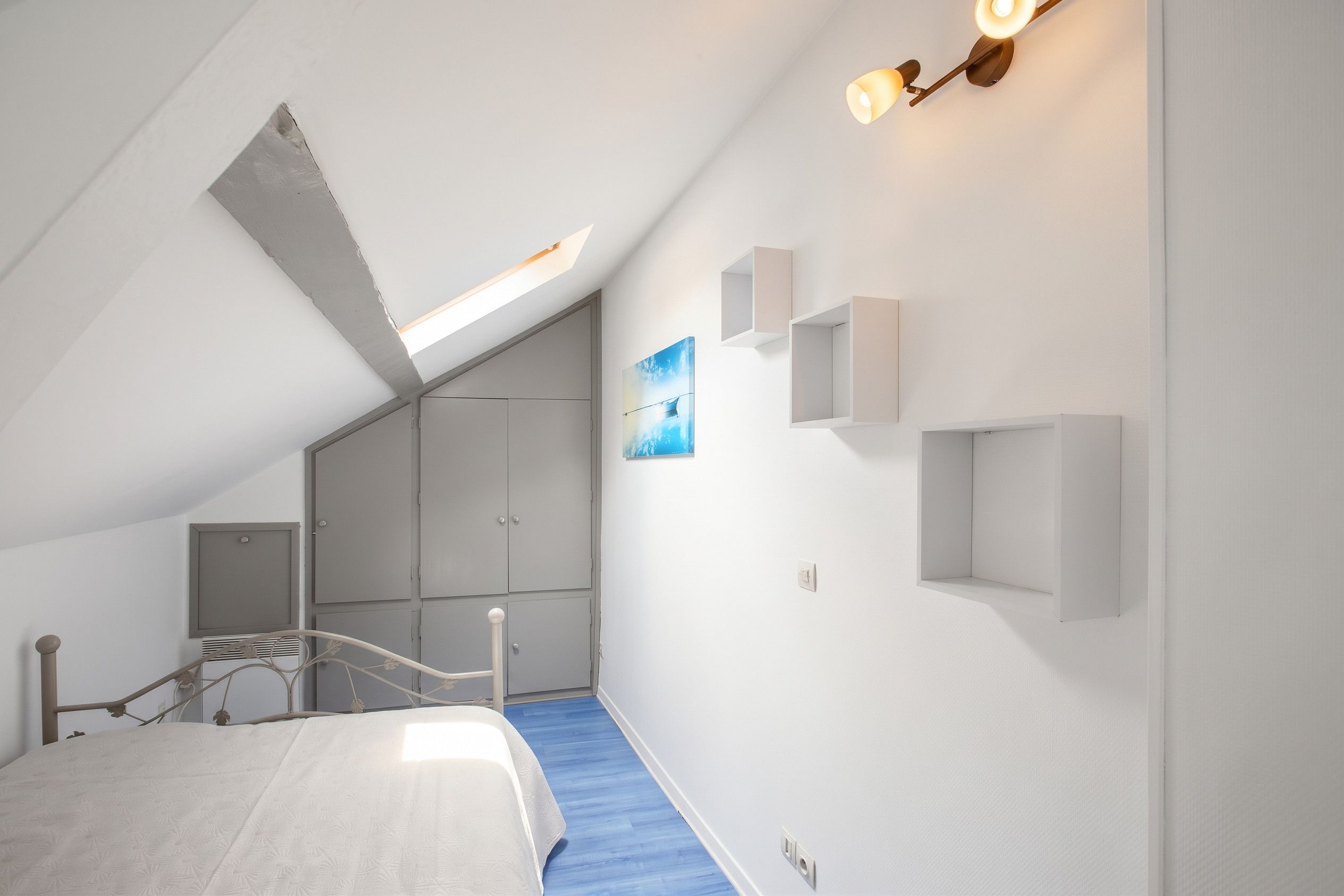 Een slaapkamer met een schuine kap, een bed, een trap en inbouwopbergkasten.