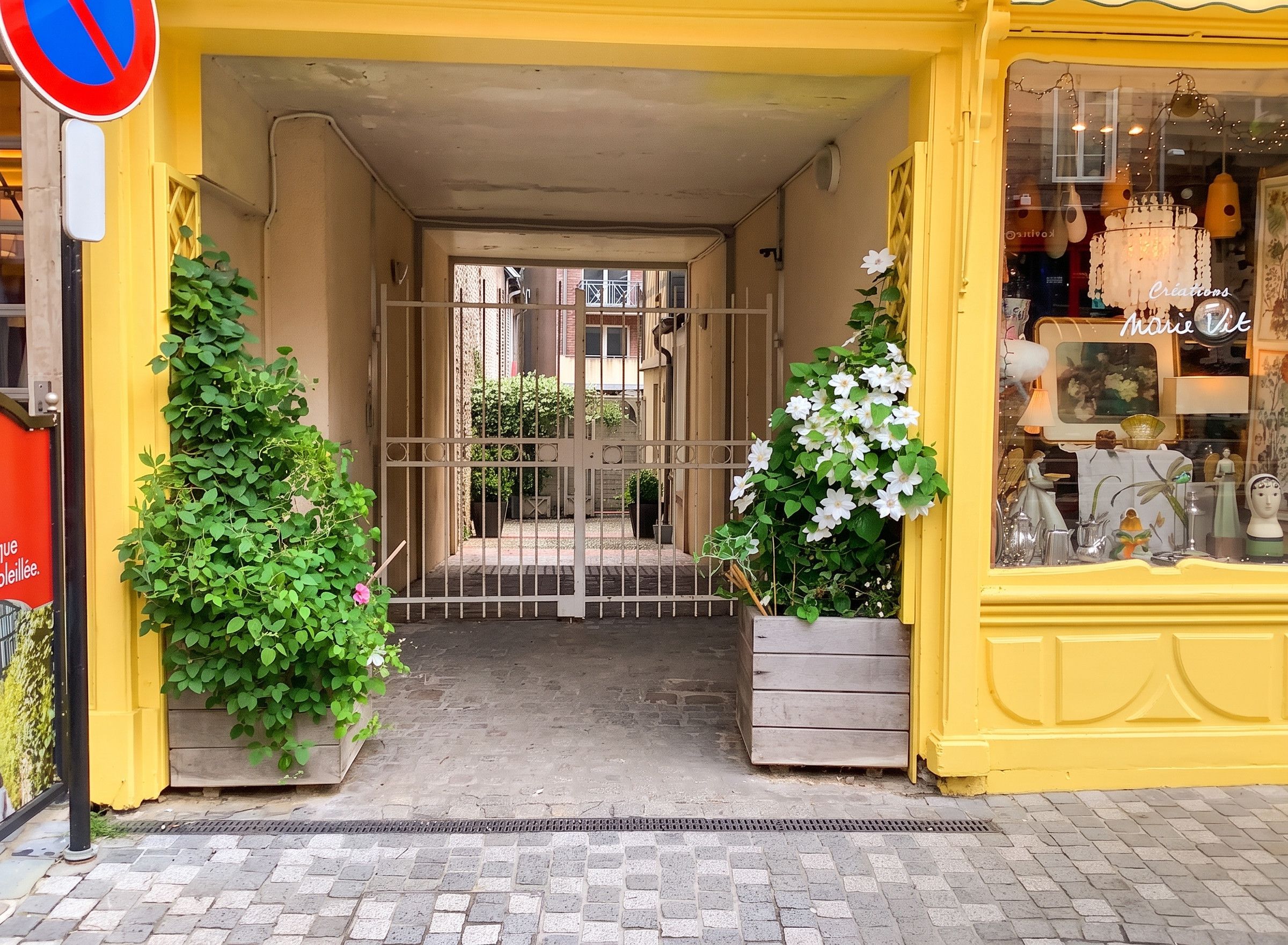 A yellow storefront with a gated entrance, potted plants, and a window display.