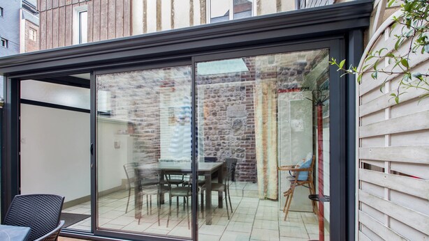 A modern patio with a glass door leading to a dining area with a table and chairs. - Homerez - Charming House near Sainte Catherine (Honfleur)