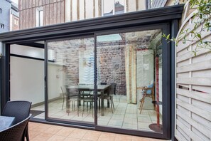 A modern patio with a glass door leading to a dining area with a table and chairs. - Homerez - Charming House near Sainte Catherine (Honfleur)