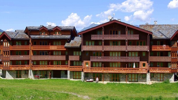 A multi-story wooden building with balconies, likely a hotel or lodge, set against a clear sky. - "Spacious 3-Room Apartment, Ski-In/Ski-Out, Sleeps 7, Forest Hamlet, Les Avanchers-Valmorel" (Valmorel)