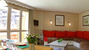 A cozy living room with a wooden dining table set for two, a sofa with red cushions, and a coffee table. - "Spacious 3-Room Apartment, Ski-In/Ski-Out, Sleeps 7, Forest Hamlet, Les Avanchers-Valmorel" (Valmorel)