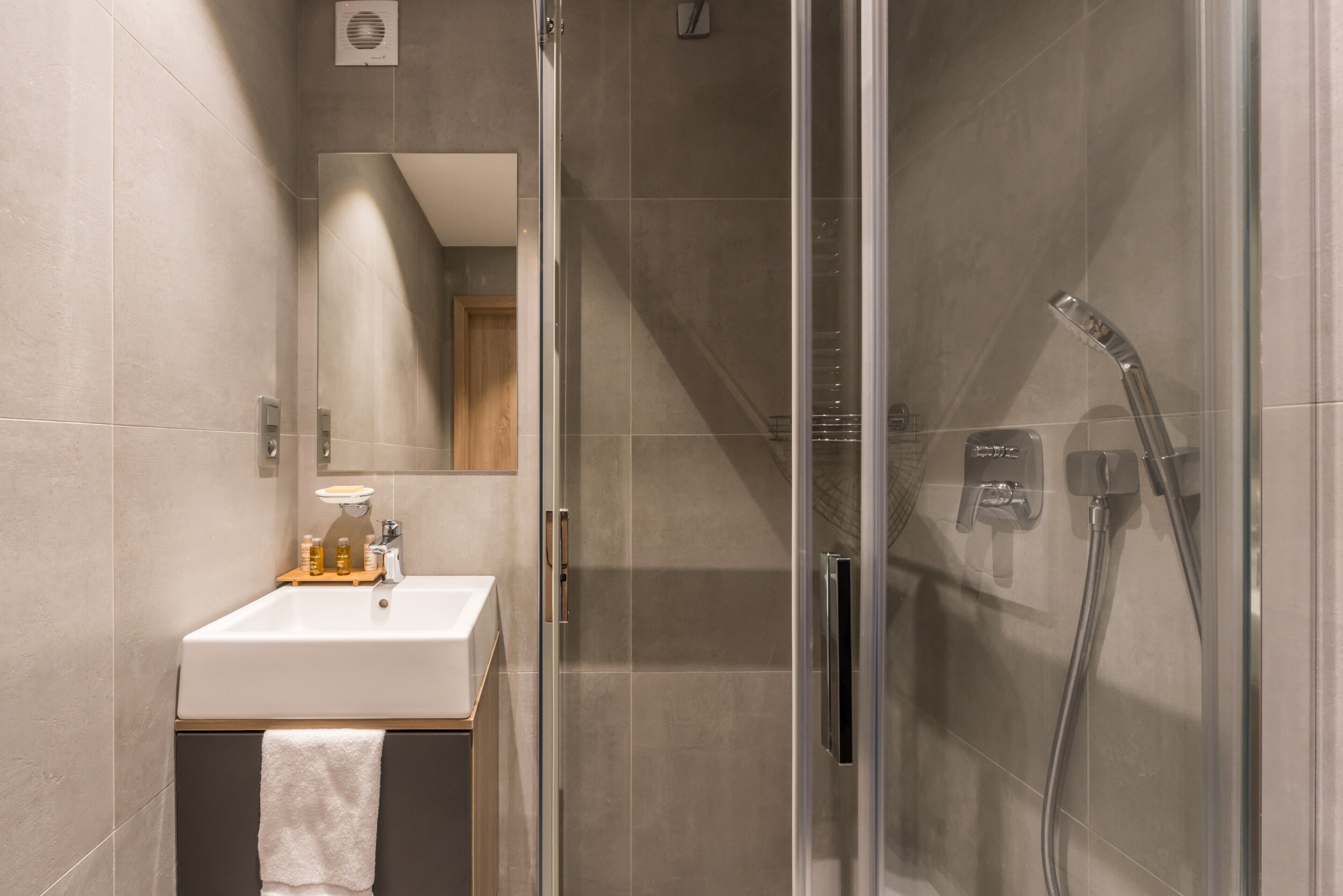 Een moderne badkamer met een douchecabine van glas, een wastafel met spiegel en een handdoek aan de deur.