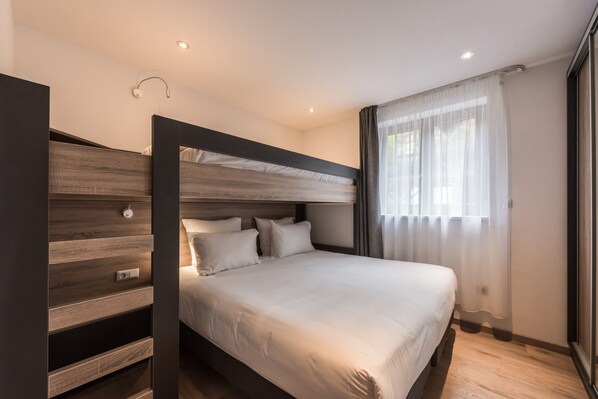 A modern bedroom with a bunk bed, a bedside table, and a window with sheer curtains.