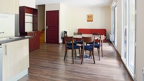 A modern kitchen with wooden cabinets, a dining area with a table and chairs, and a red door.