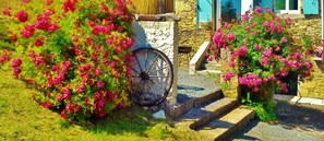 En stentrappe fører op til en bygning, hvor der står en trillebør og lyserøde blomster står i bed.