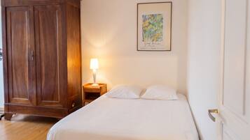 A hotel room with a bed, a nightstand with a lamp, a wardrobe, and a framed picture on the wall.