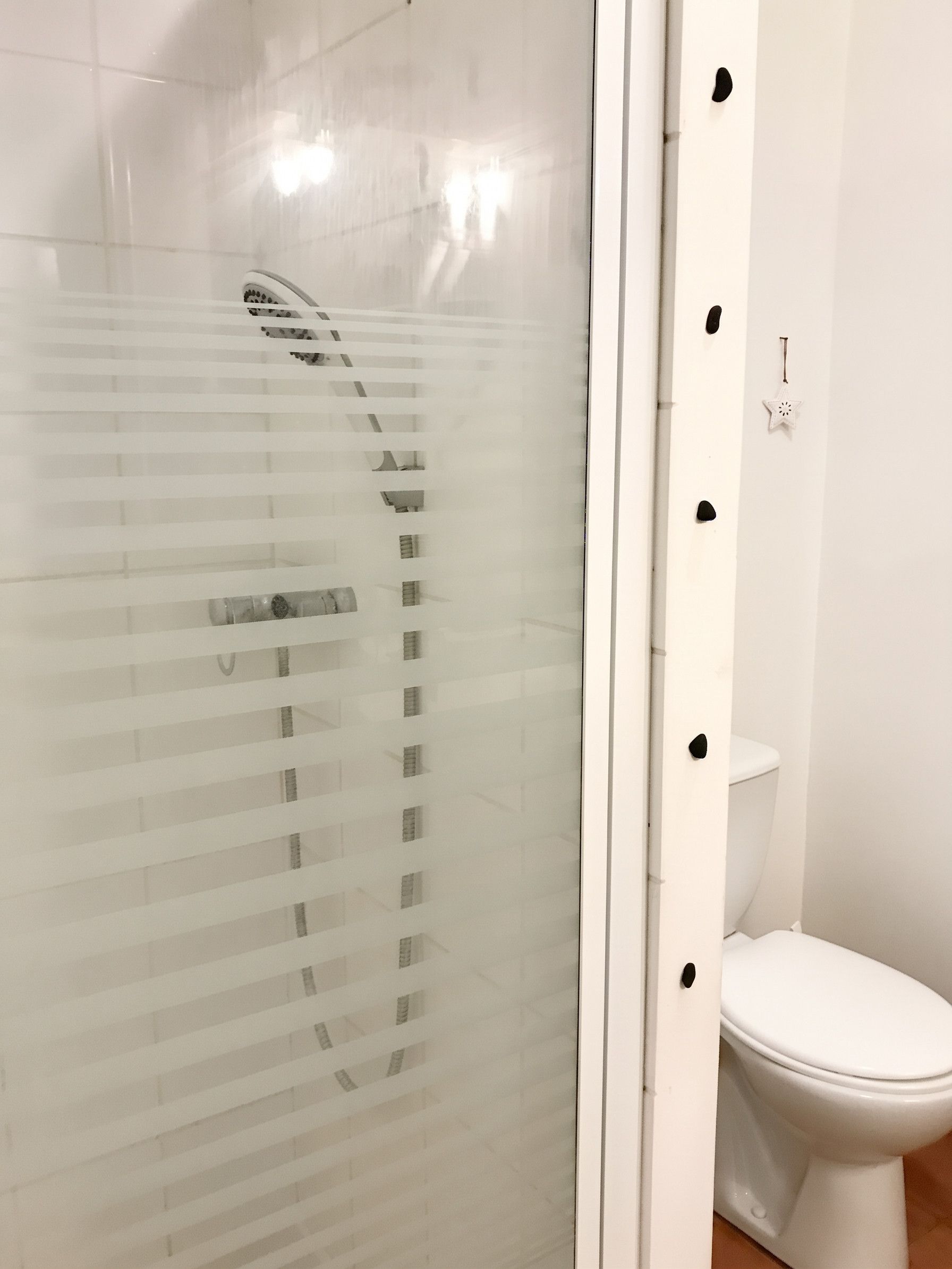 Un baño con cabina de ducha de vidrio, un inodoro blanco y una pared blanca con un adorno con forma de estrella.