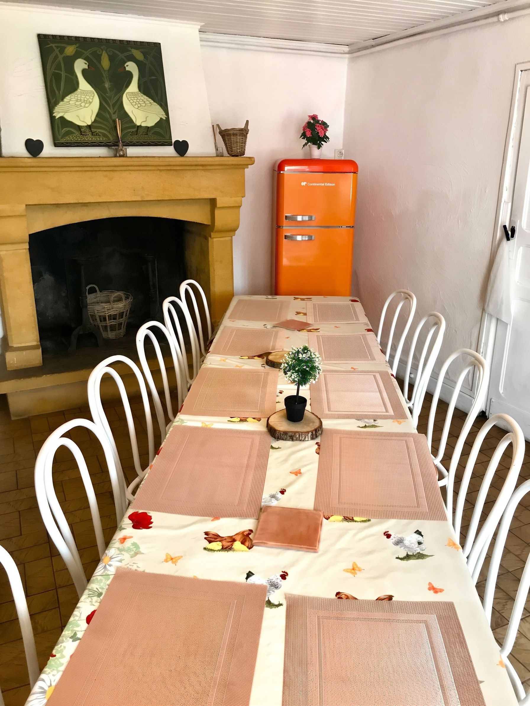 A dining room with a long table, white chairs, a fireplace, and an orange appliance.