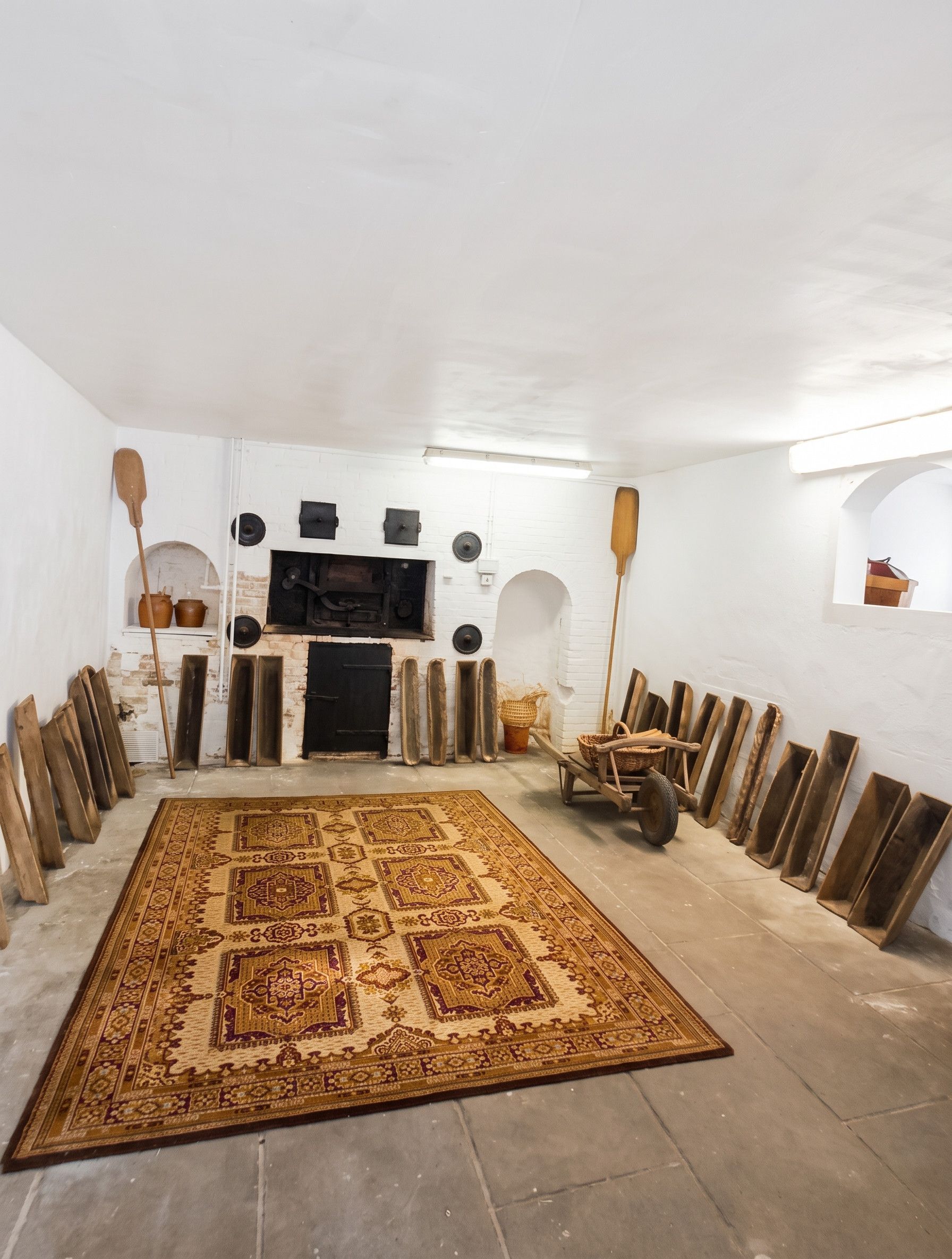 A room with a large patterned rug, a fireplace, and various wooden objects.