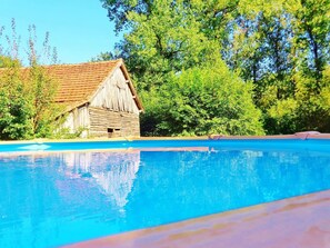 En swimmingpool med et træværksted og frodig vegetation i baggrunden.