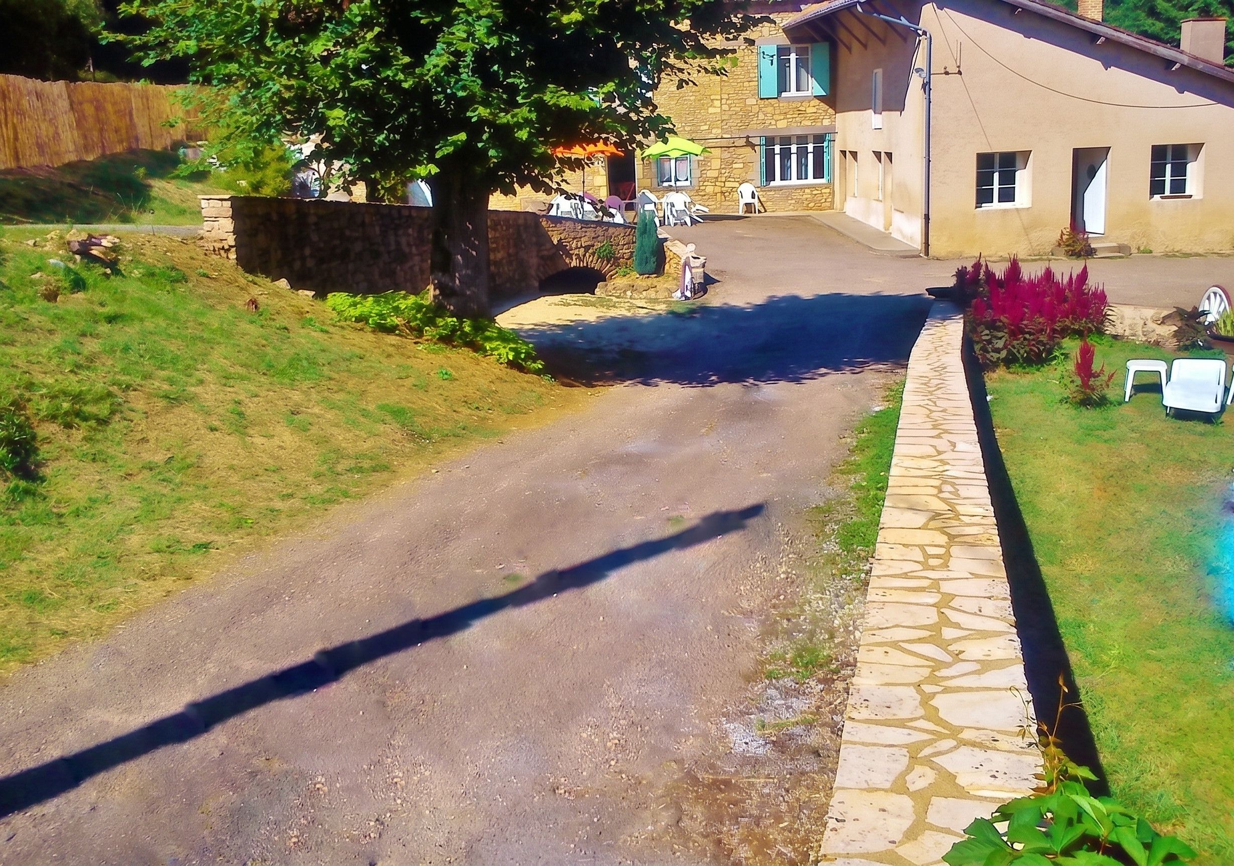 Une rue résidentielle avec un chemin pavé de pierres, une zone herbeuse et une maison à la façade en pierre.