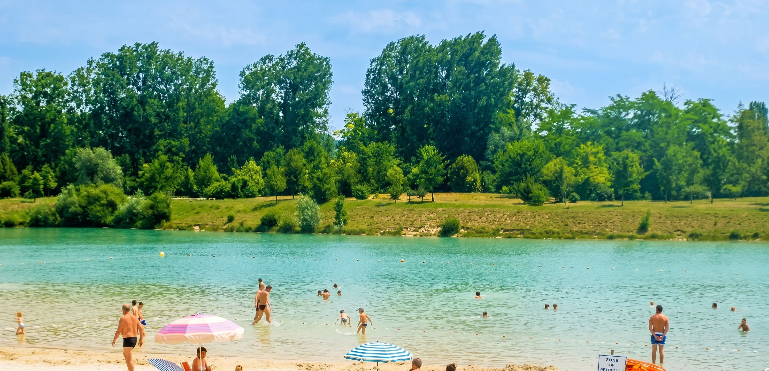 Ein Strand mit badenden und spazierenden Menschen, umgeben von Bäumen.