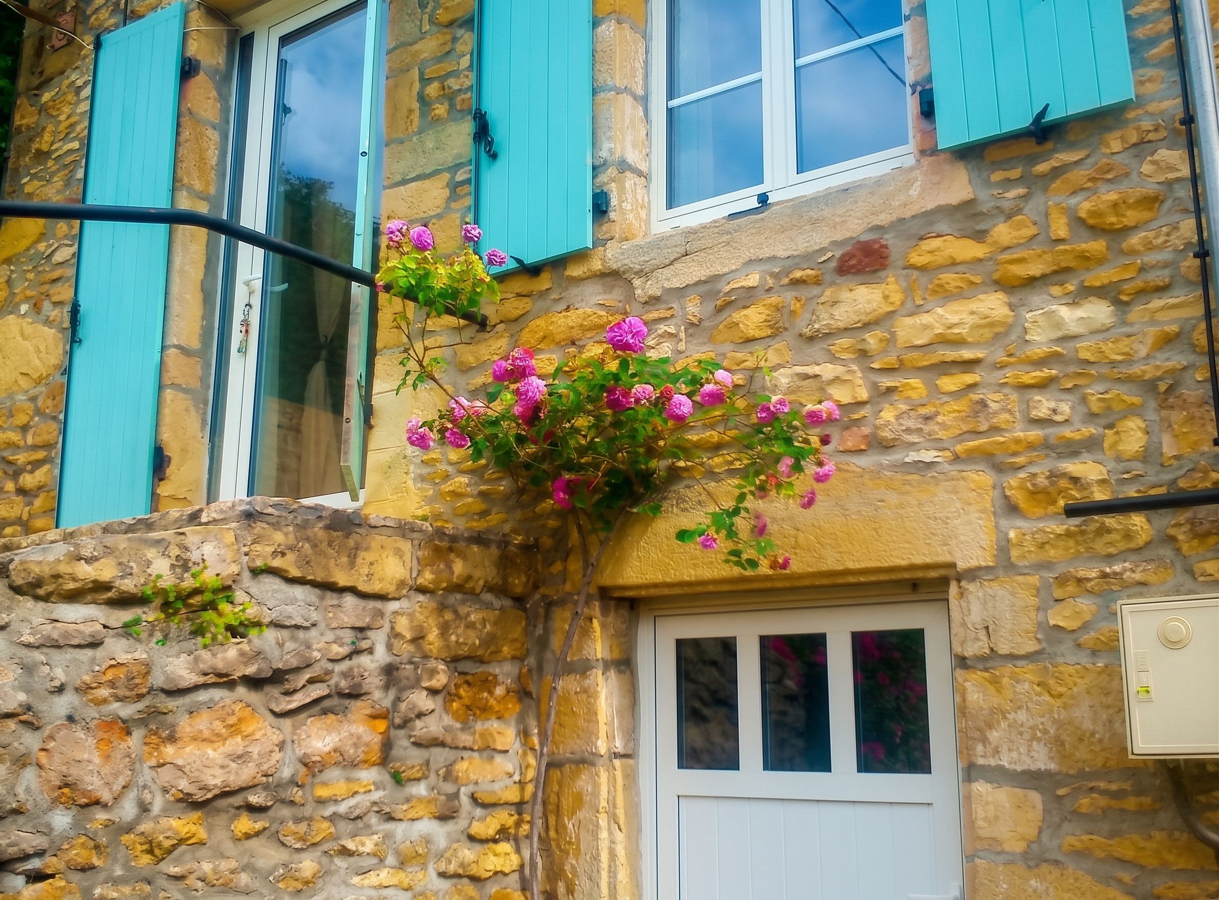A stone building with a white door and turquoise shutters.