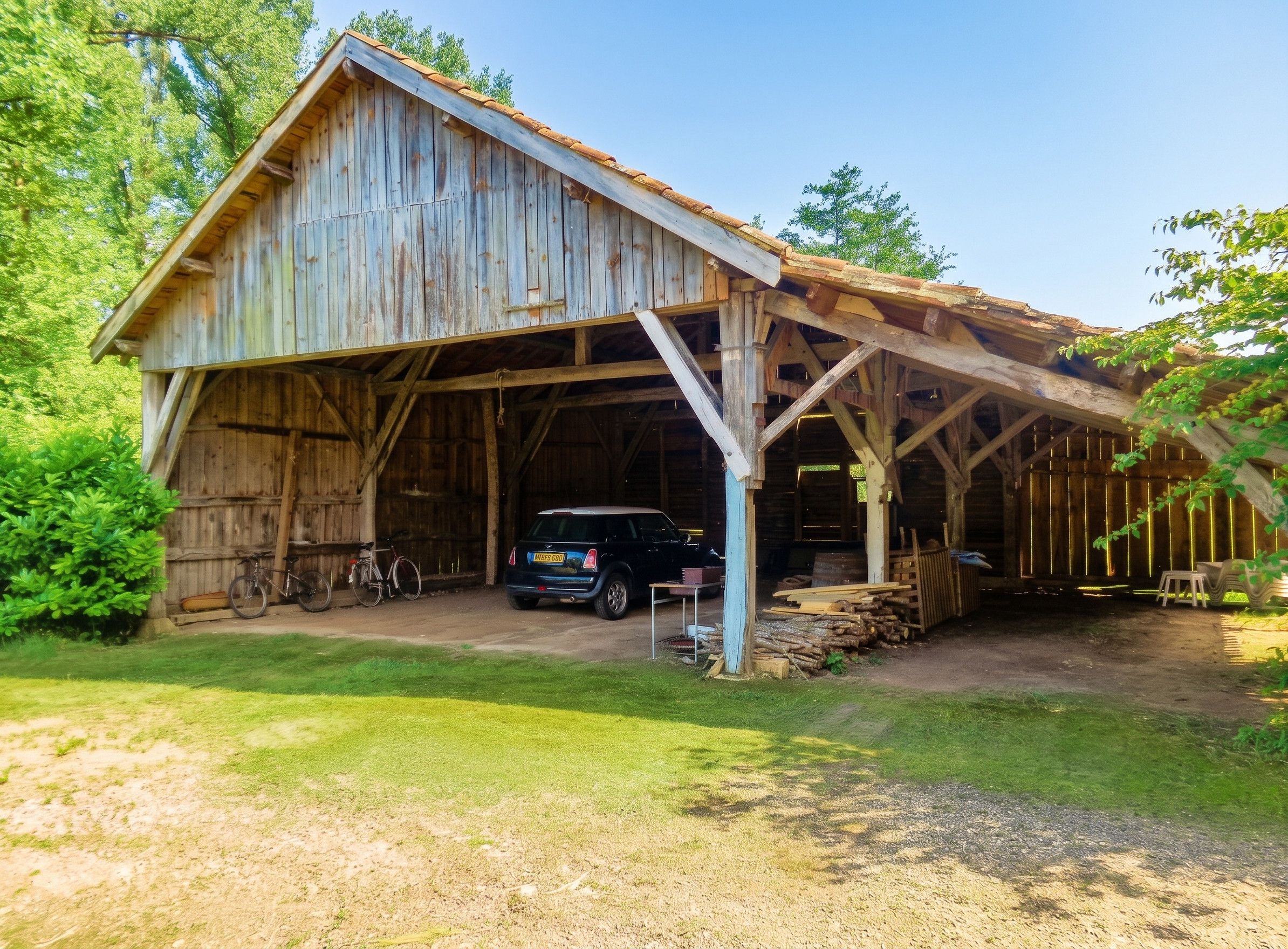 A rustic barn with a covered entrance, a car parked inside, and a bicycle leaning against the wall.